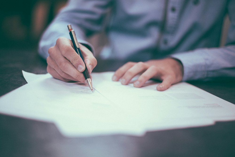 Una persona firma documentos sobre una mesa