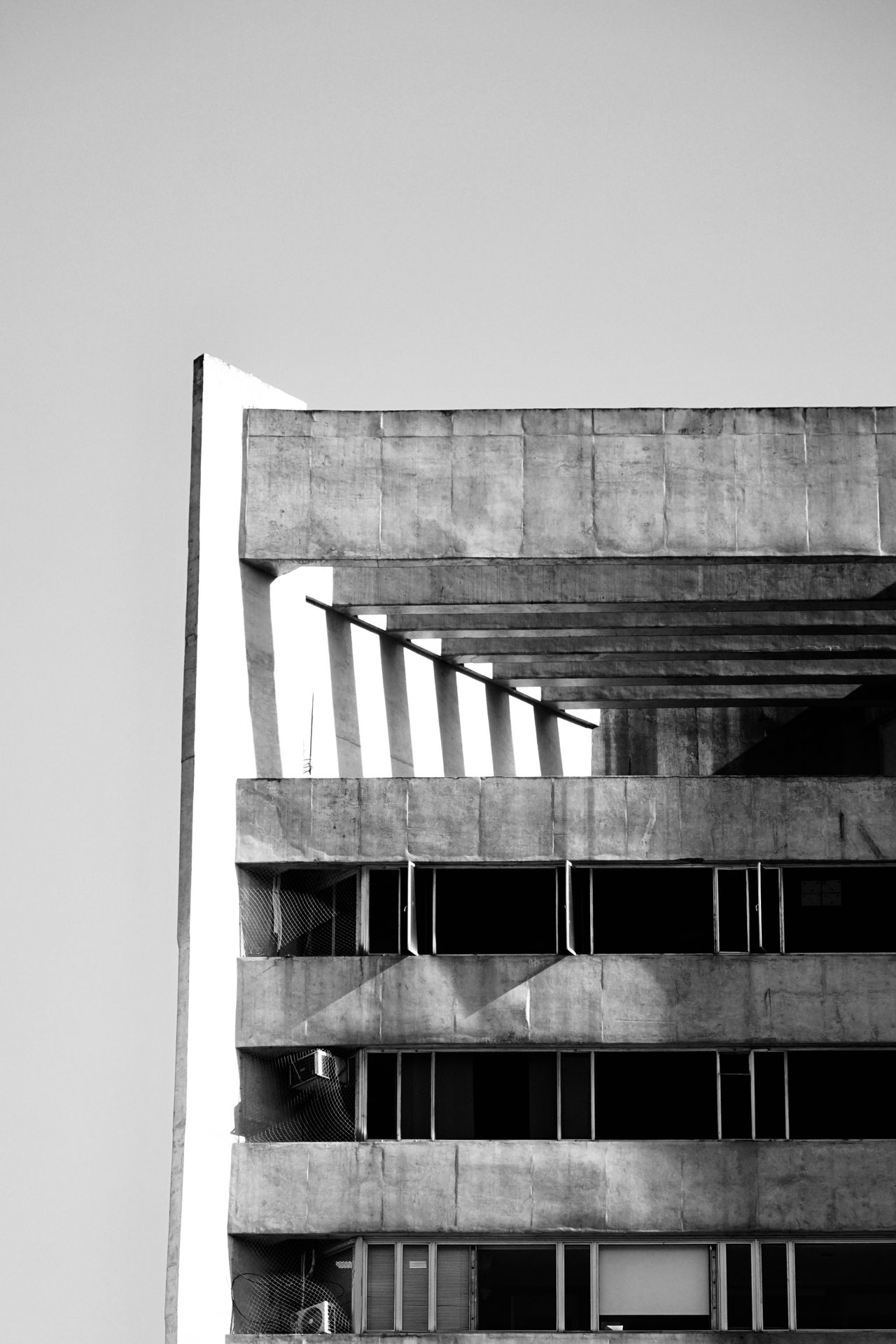 Esquina de un edificio brutalista de hormigón contra un cielo claro, en blanco y negro