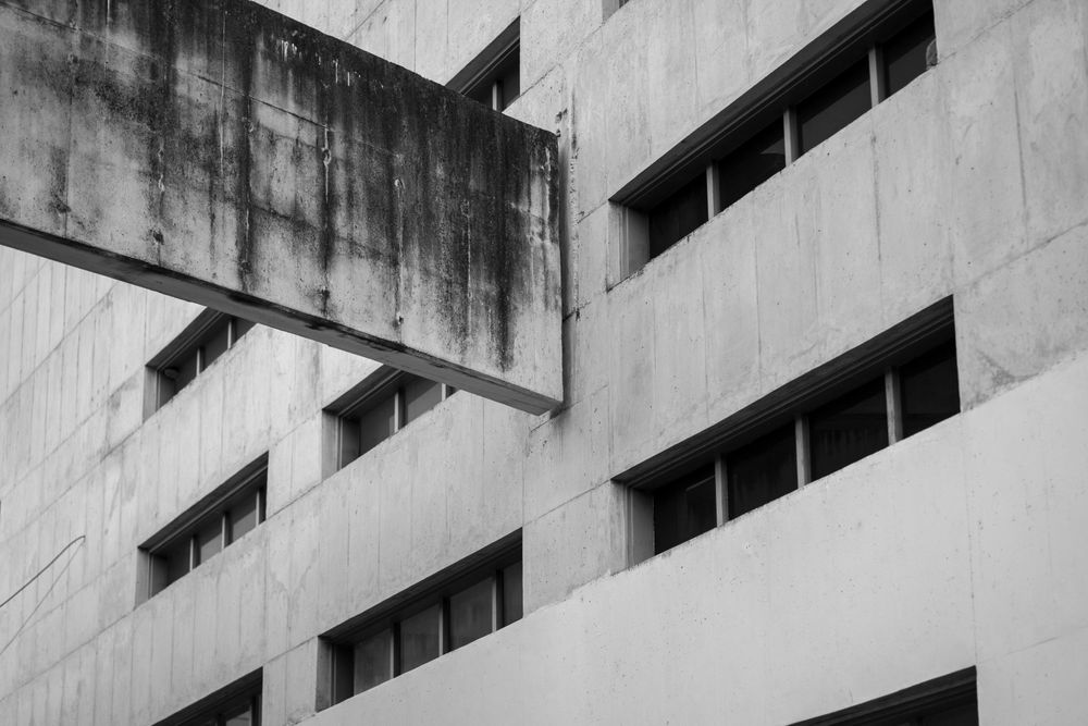 Fachada de hormigón con ventanas horizontales en línea y un volumen que sobresale, en blanco y negro